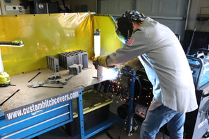 Shawn welding metal components in a workshop with protective yellow curtain.